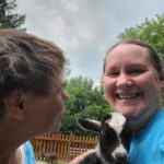 Heather from our Community Habilitation program holds a baby goat while supported individual Michelle pets the goat. 