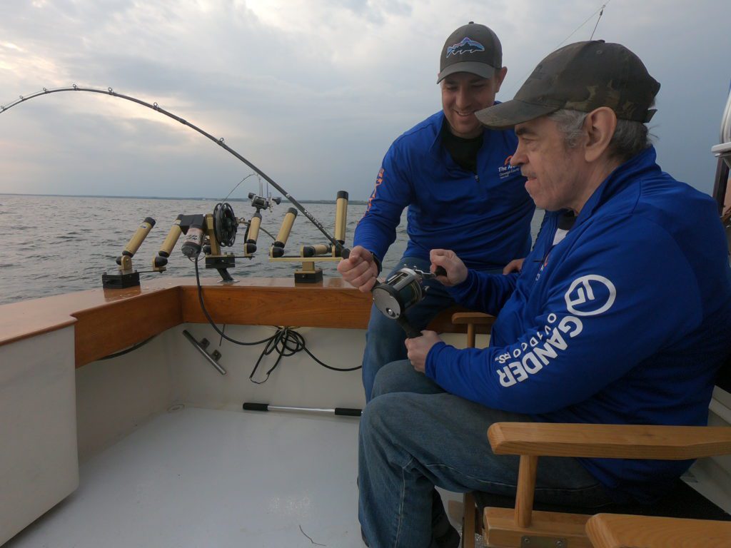 Respite staff assisting an older man with disabilities in fishing for king salmon on a fishing charter