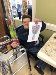 An adult woman with disabilities holds up a completed coloring page showing a bouquet of flowers
